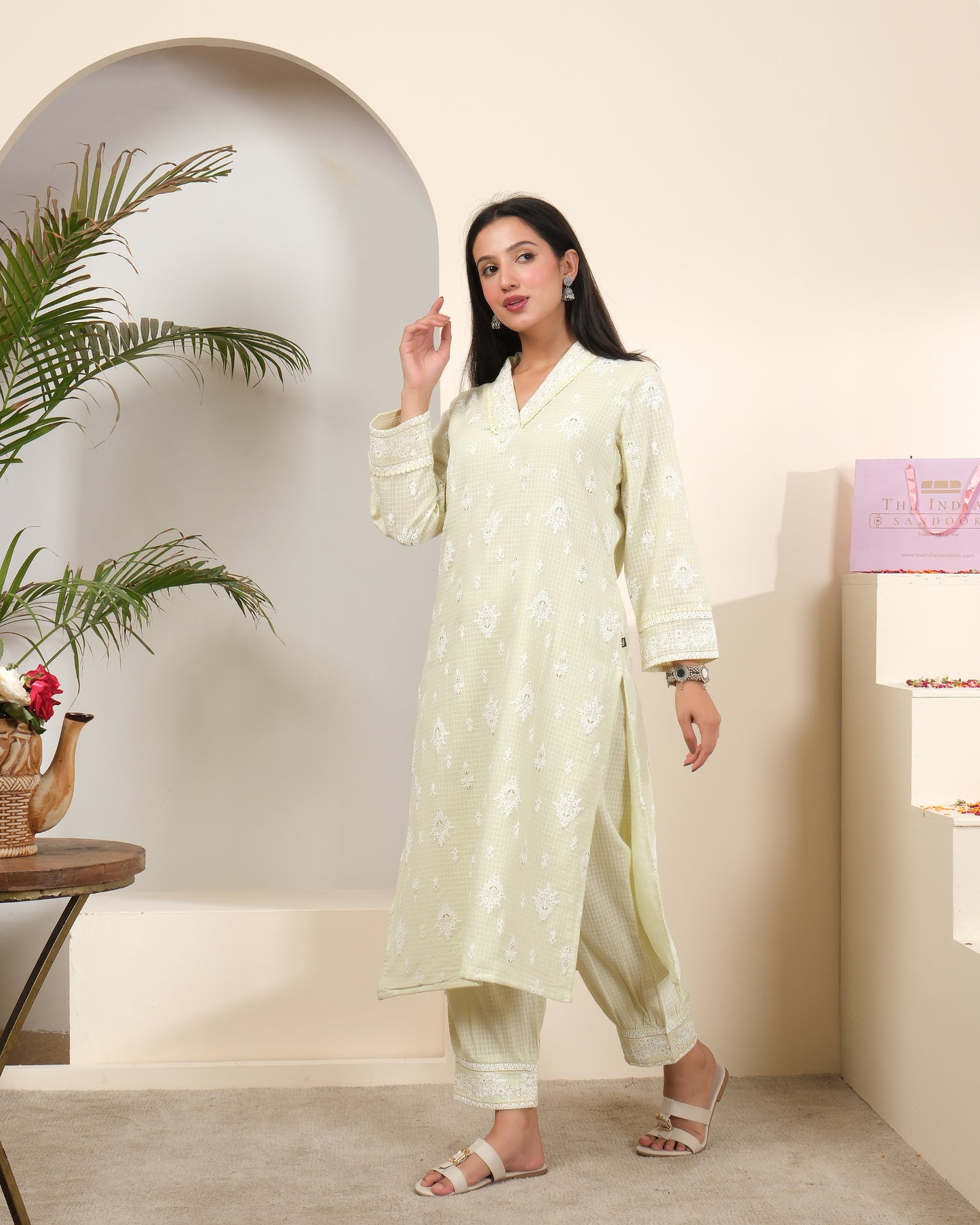 A woman posing in a pastel sage green cotton kurta pant set with a sheer, shimmering striped dupatta featuring tassels