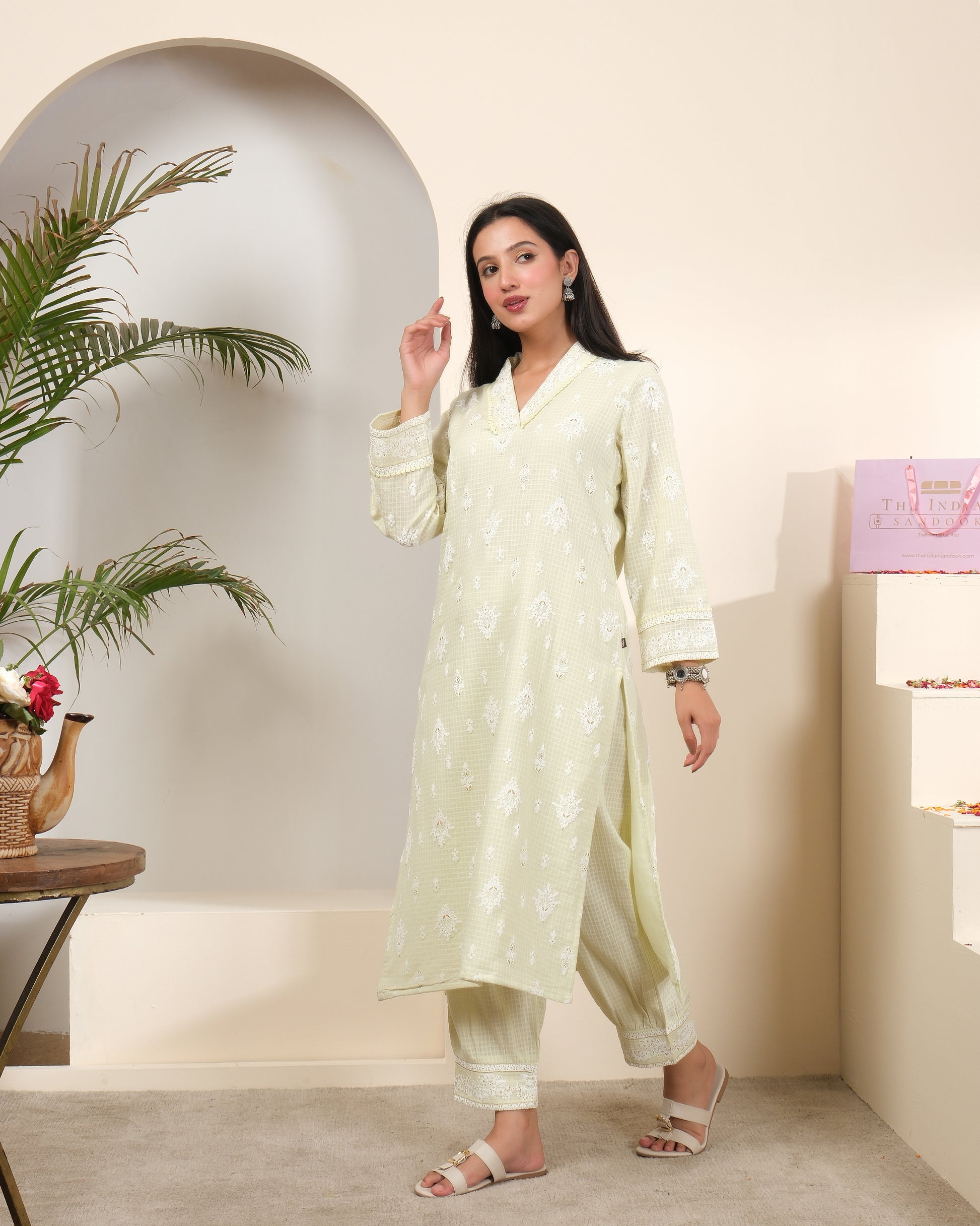 A woman posing in a pastel sage green cotton kurta pant set with a sheer, shimmering striped dupatta featuring tassels