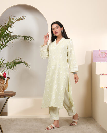 A woman posing in a pastel sage green cotton kurta pant set with a sheer, shimmering striped dupatta featuring tassels