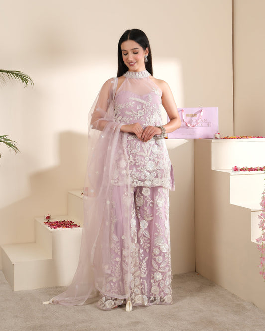 Woman in a light purple floral dress standing in a softly lit room.