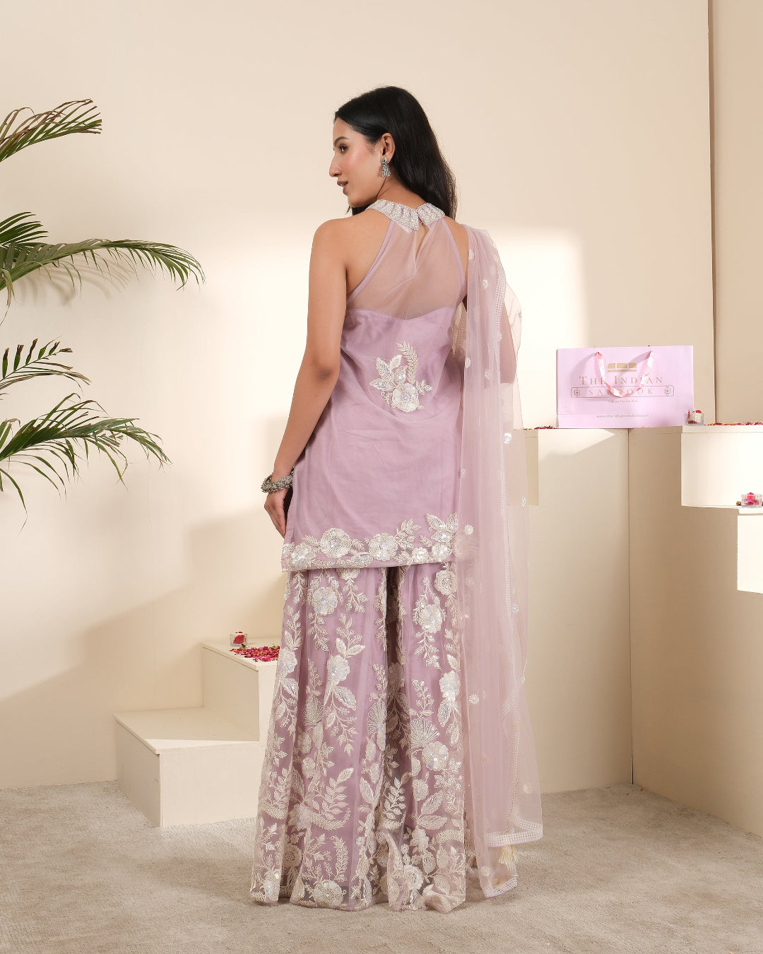 Woman in a light purple saree with white floral patterns in a room setting.